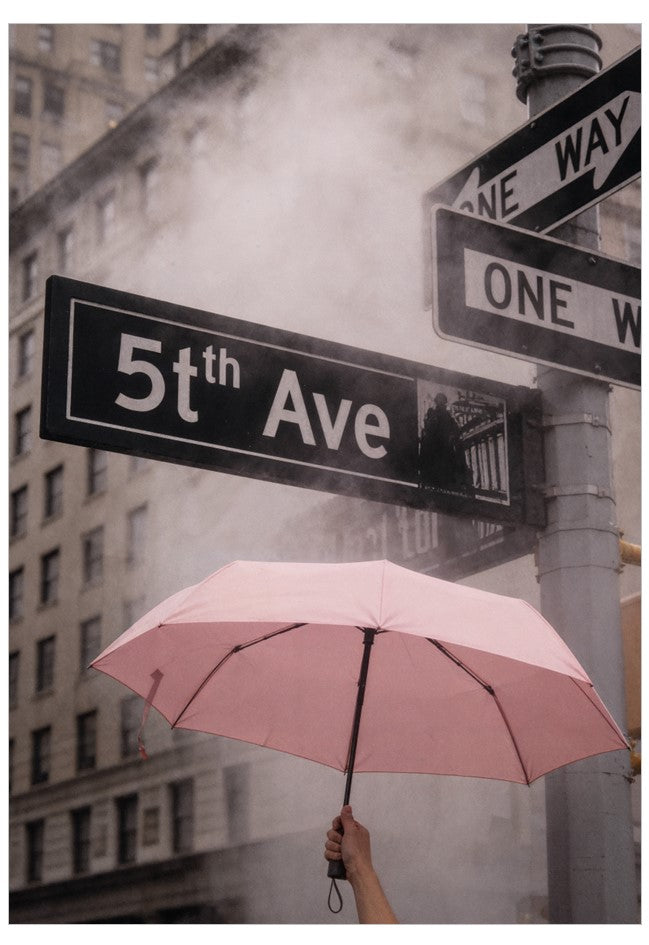 Pink umbrella held over a street sign for 5th Ave in an urban setting with smoke.
