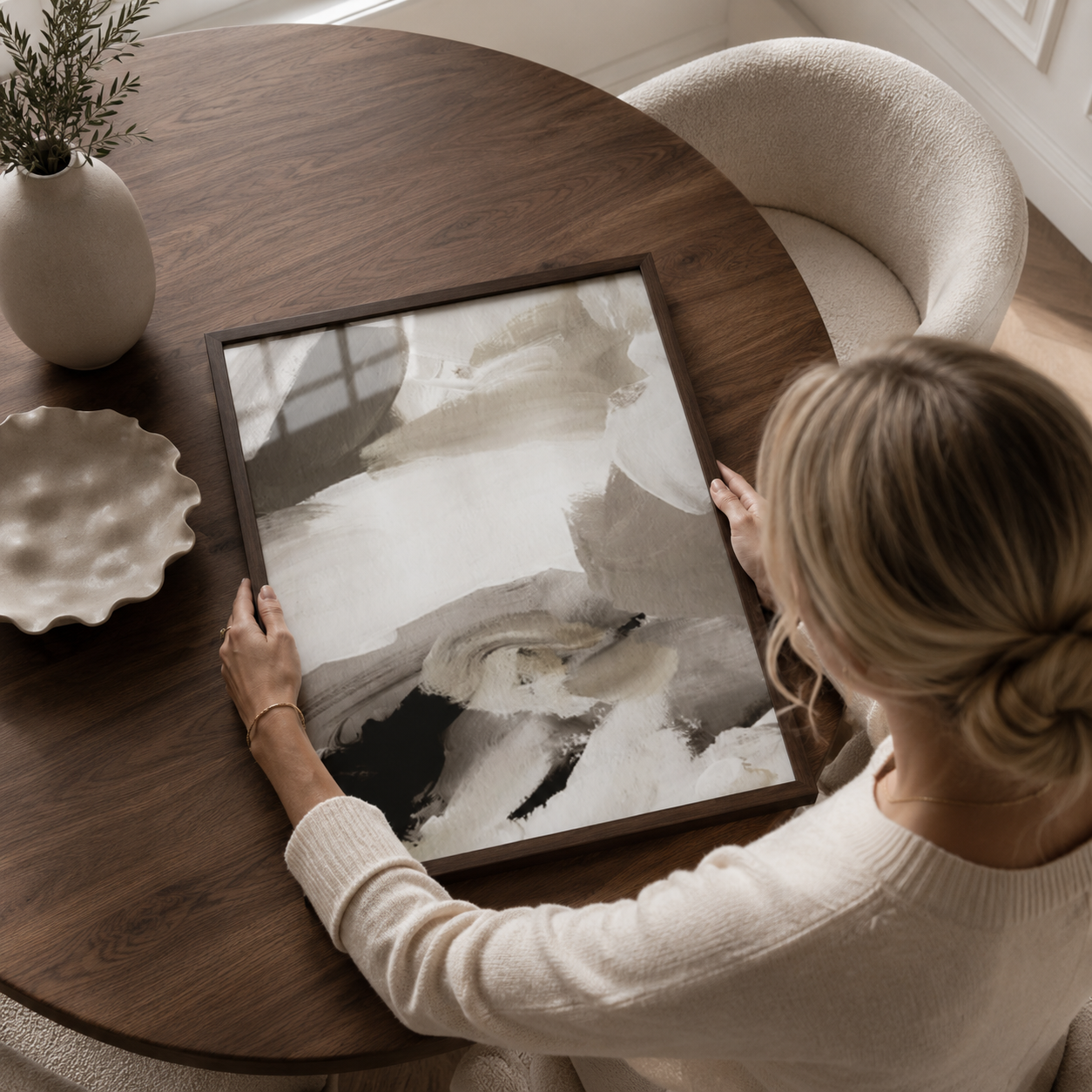 Woman arranging a framed abstract painting on a wooden table.