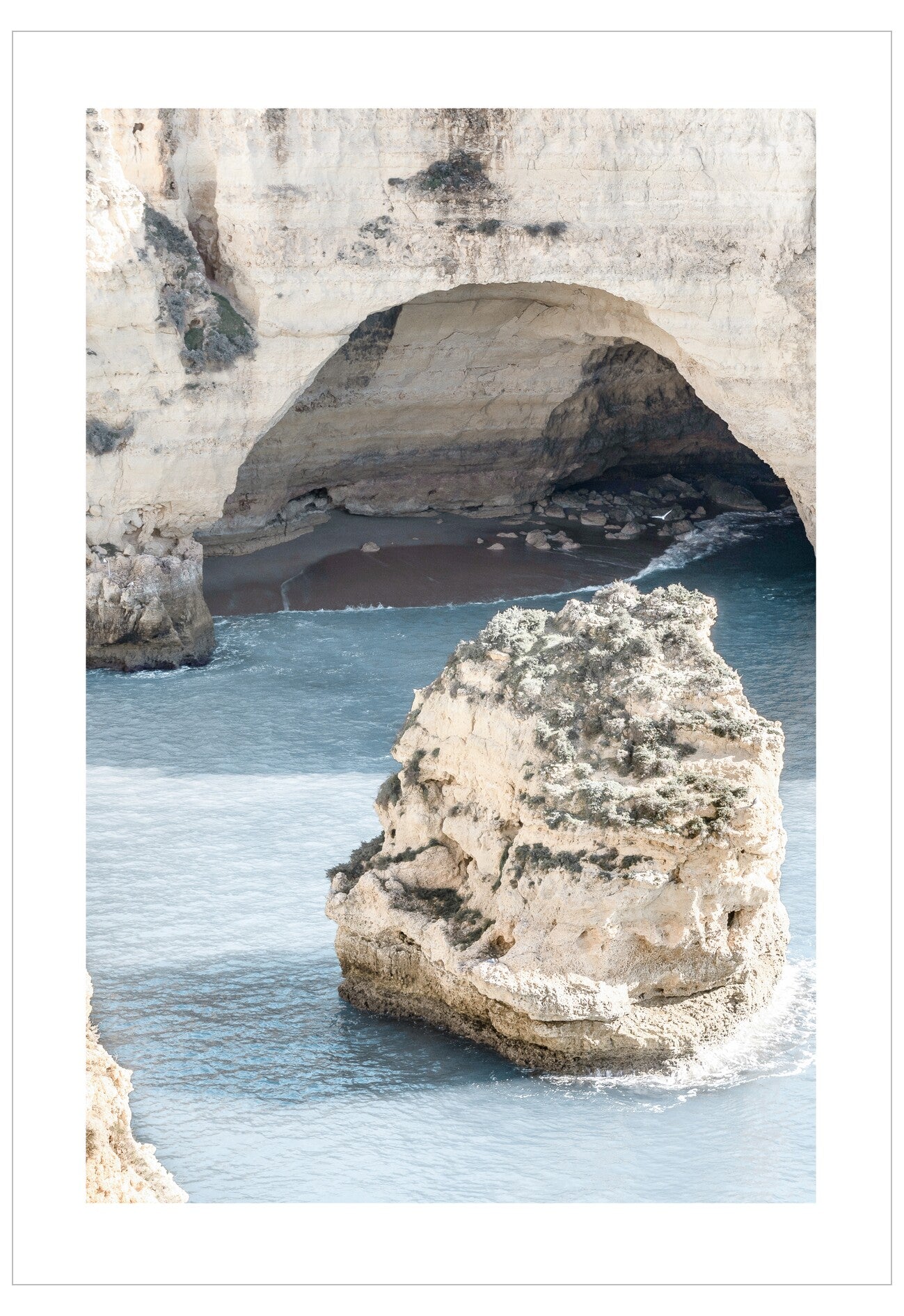 Cave entrance with a rock formation in the foreground, surrounded by water.