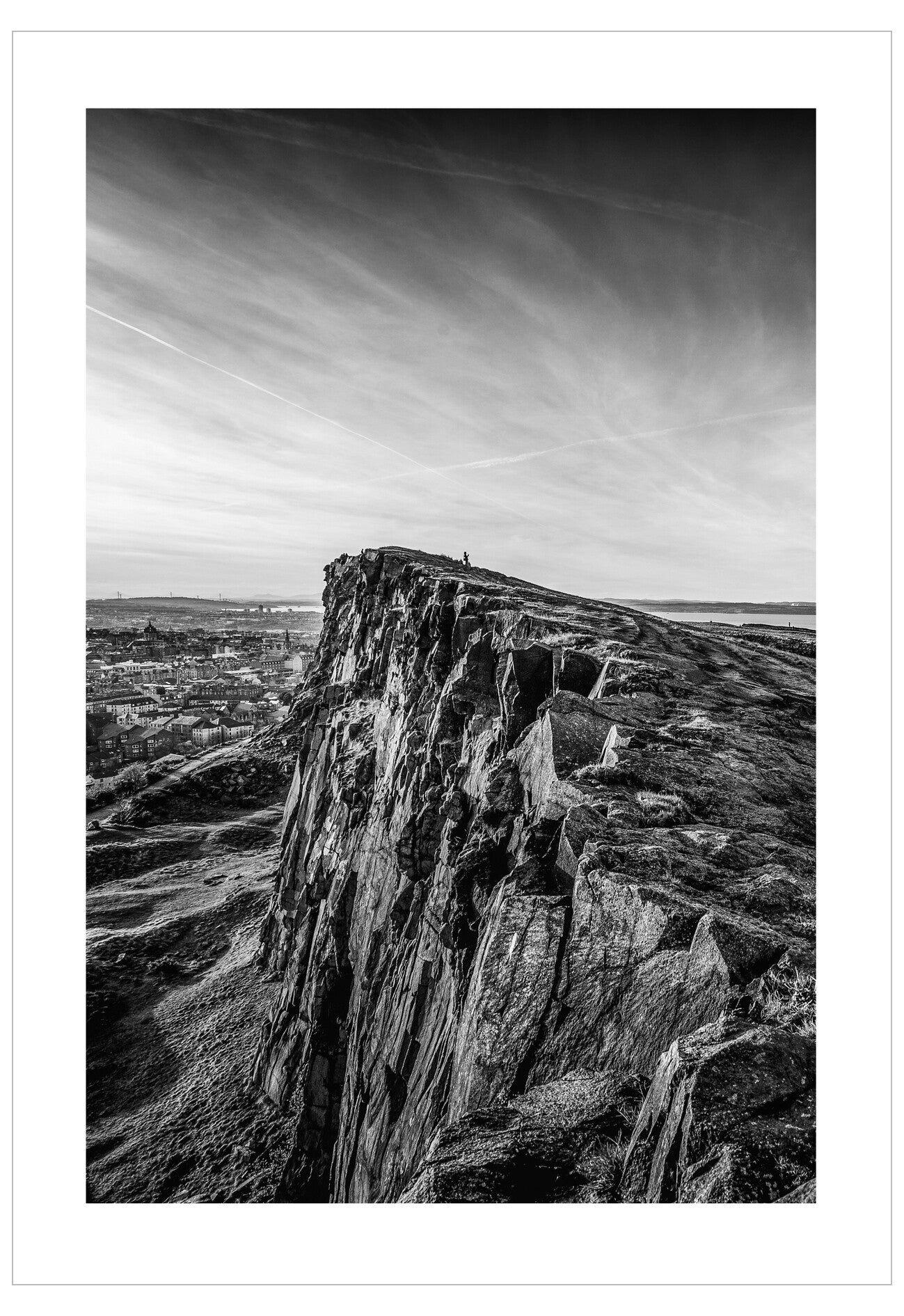 Black and white photograph of a large rocky outcrop with a landscape in the background