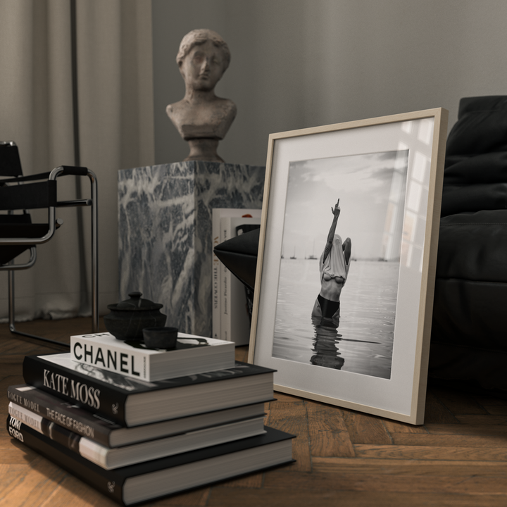 Stack of books with a Chanel book, framed black and white photo, and bust in a room setting.