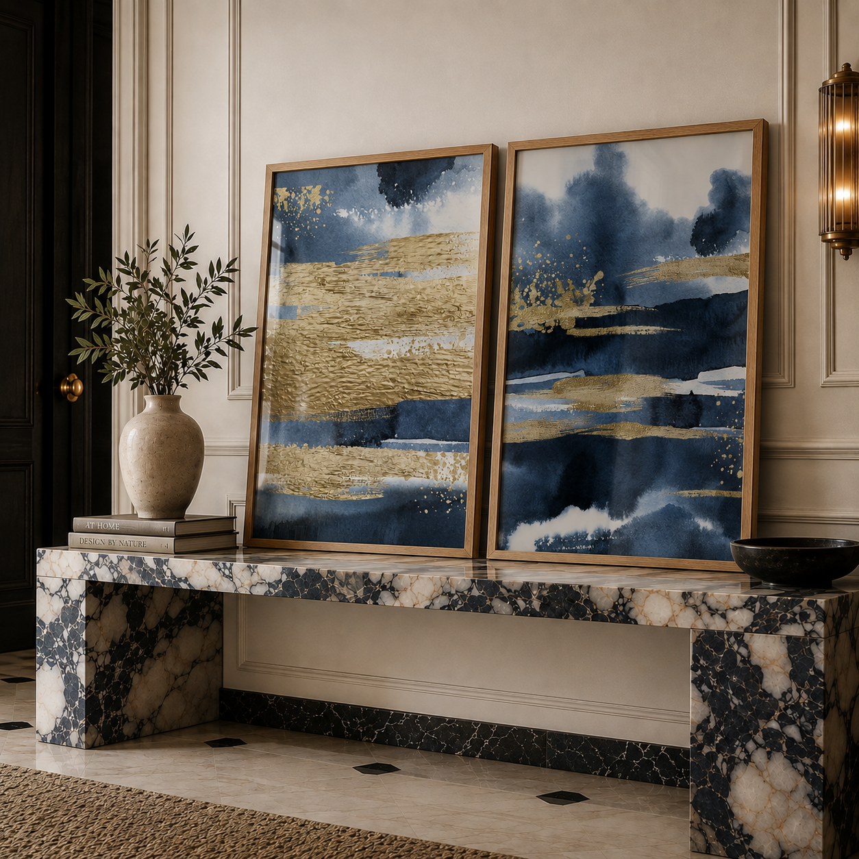 Two framed abstract wall art prints with navy blue, gold, and white brushstrokes displayed on a marble console bench in an elegant interior setting.