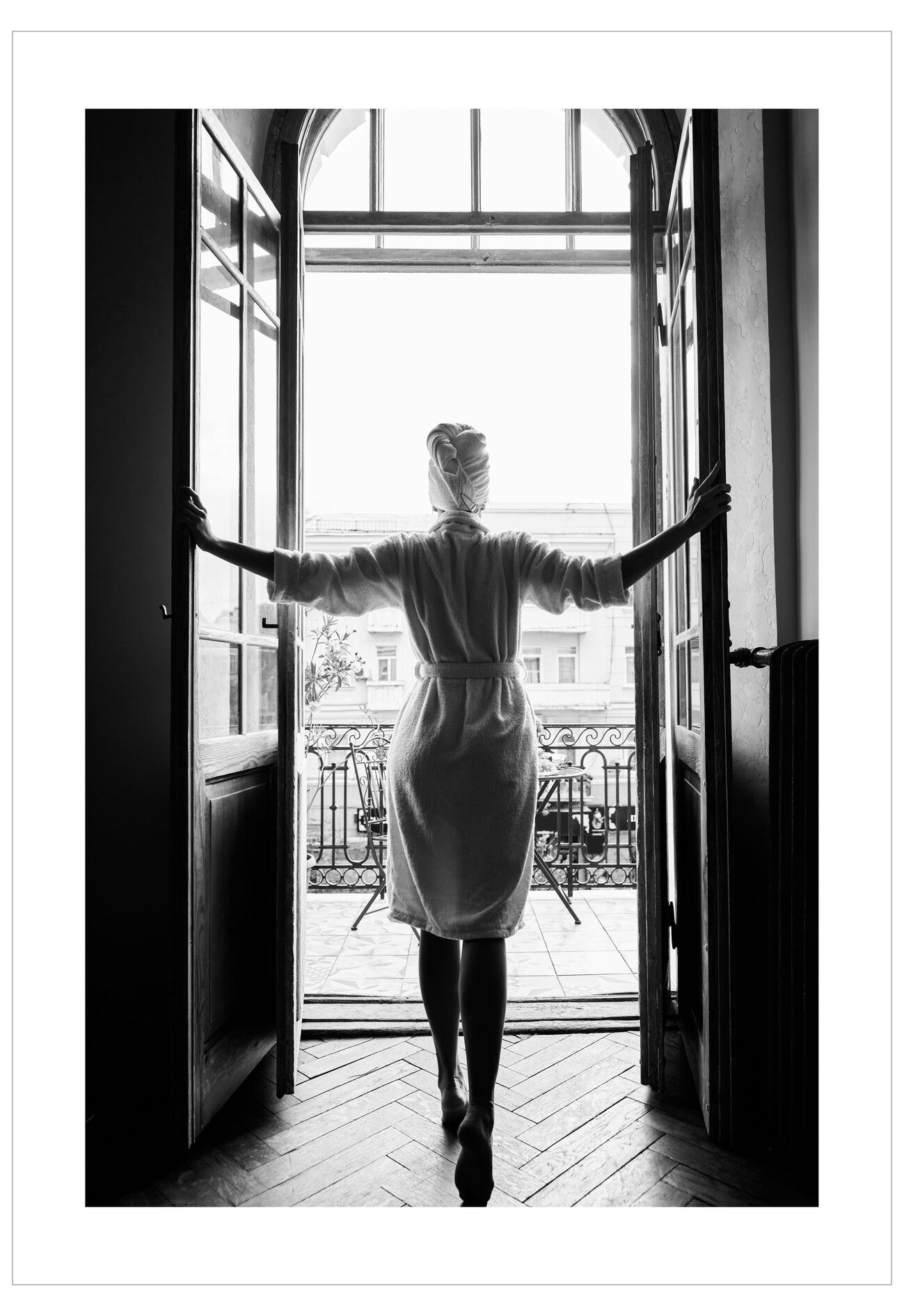 Person in a white coat standing in a doorway with arms outstretched, looking out onto a balcony.