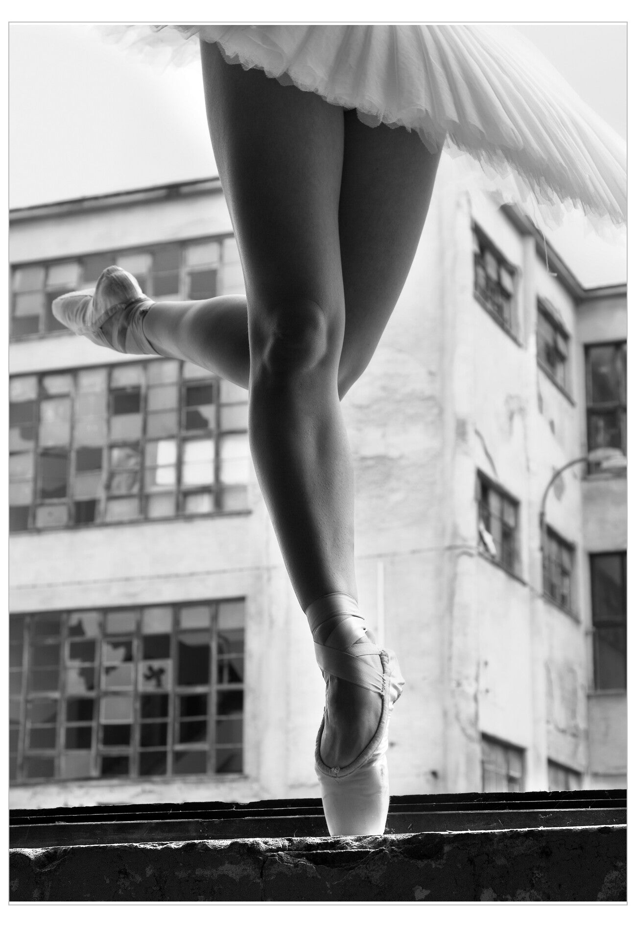 Ballerina in a tutu and pointe shoes standing on one leg with a cityscape background