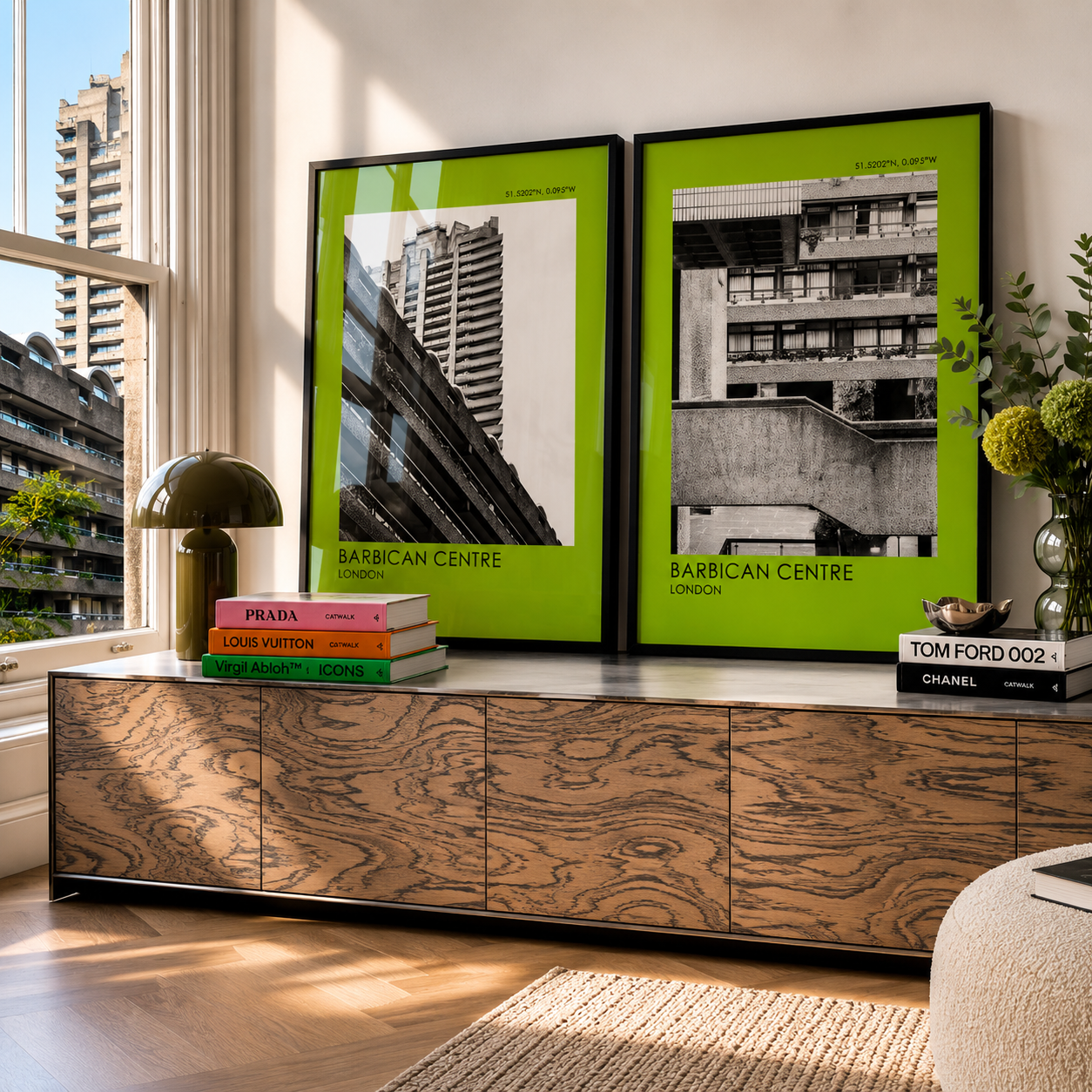 Wooden cabinet with framed Barbican Centre prints and books in a room with large windows.
