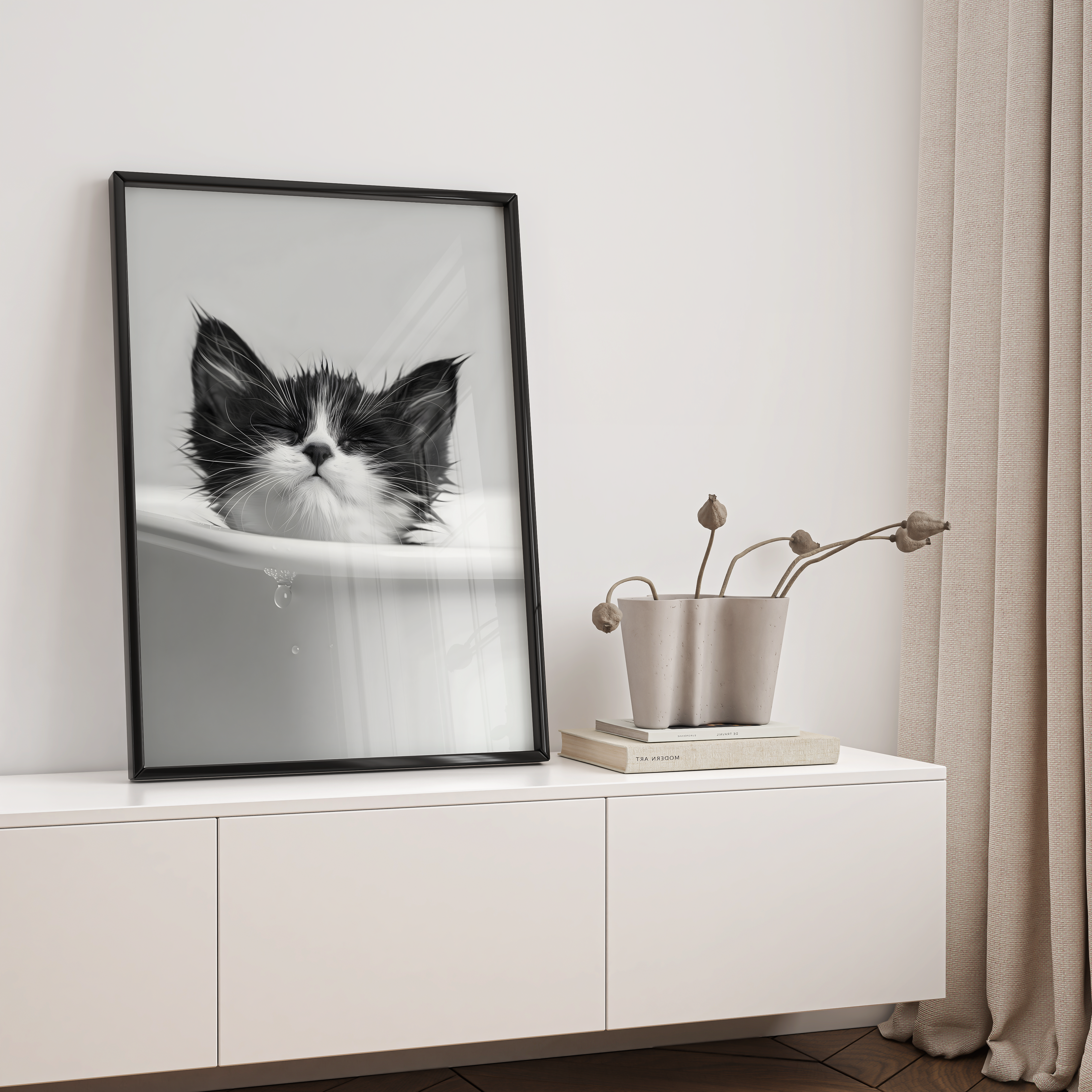 Framed black and white cat print on a white wall above a white cabinet with decorative items.