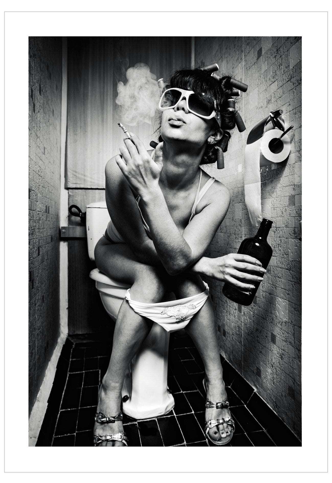 Person sitting on a toilet in a bathroom, holding a bottle and smoking a cigarette.