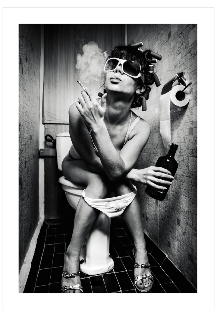 Person sitting on a toilet in a bathroom, holding a bottle and smoking a cigarette.