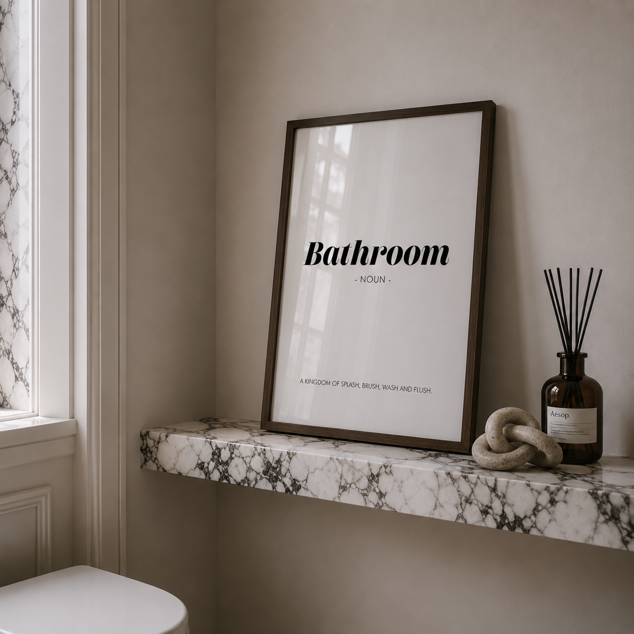 Framed poster with 'Bathroom' definition on a marble shelf with decorative items.
