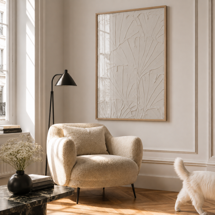 Beige armchair in a living room with abstract art on the wall and a cat walking by.