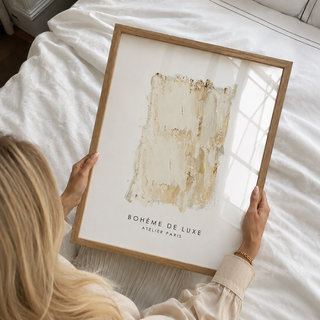 Person holding a framed artwork titled 'Bohéme de Luxe' by Atelier Paris on a bed.