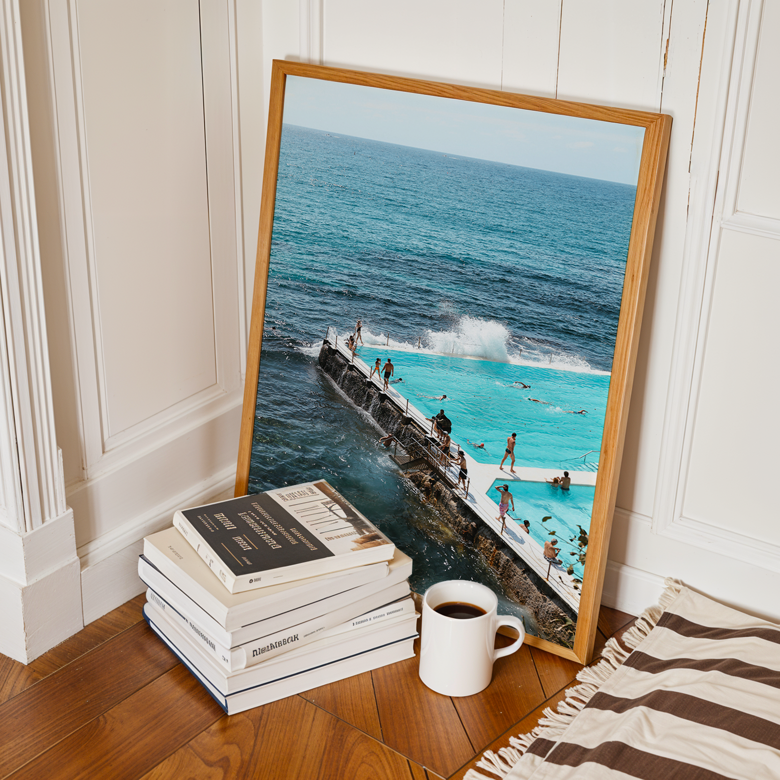 Framed photograph of a pool with people next to a body of water, placed on a stack of books with a cup beside it.