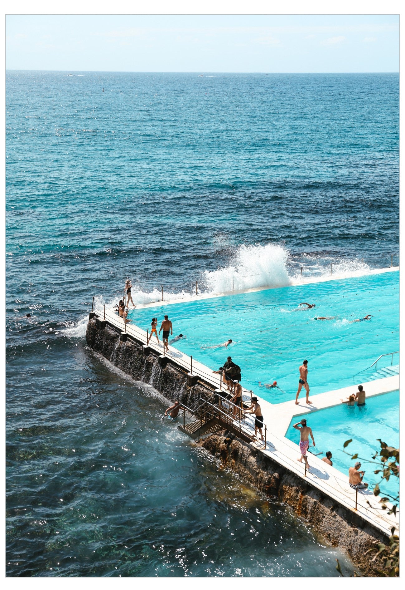 People enjoying Bondi pool next to the ocean with clear blue water and a bright sky.