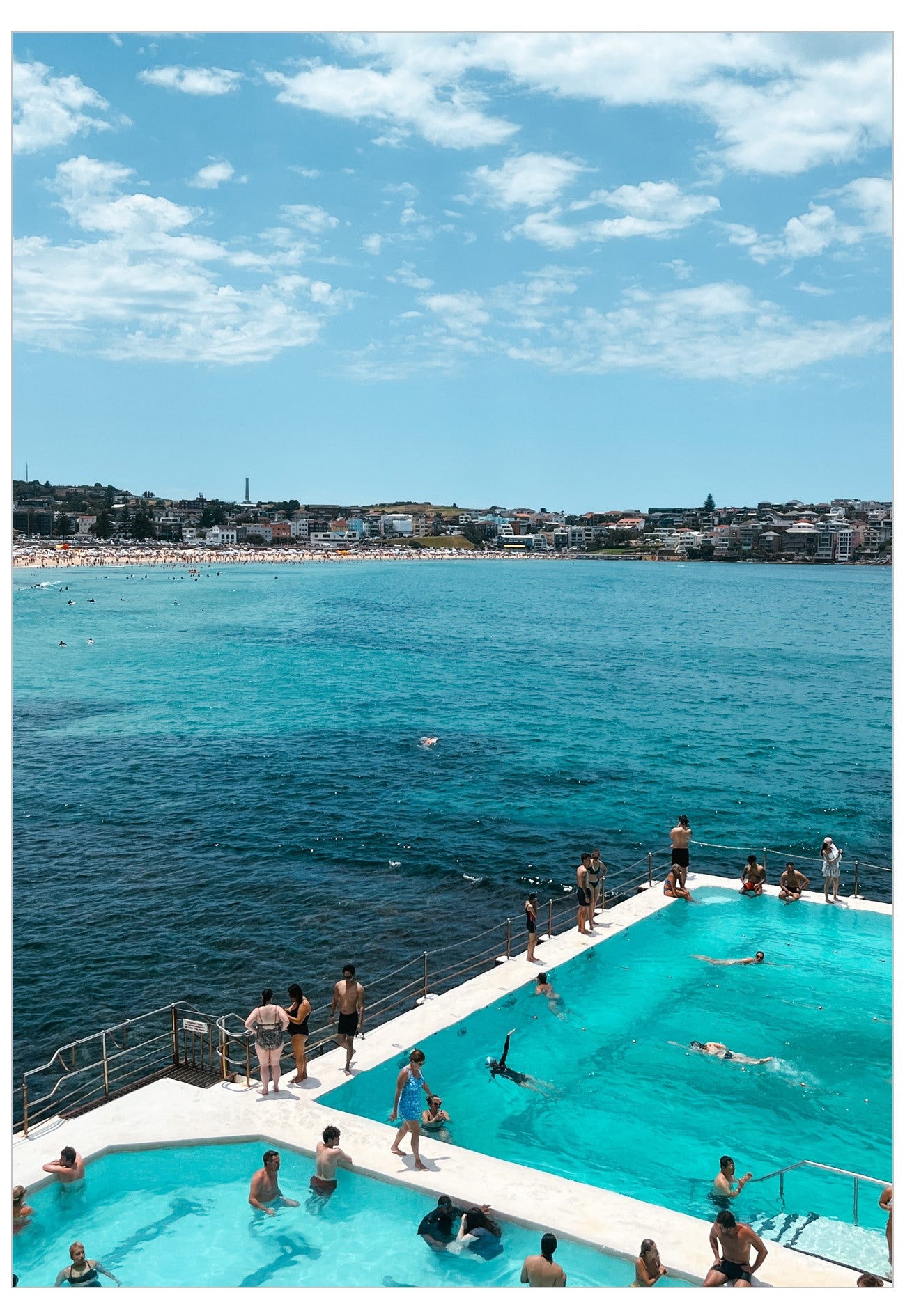 People enjoying a pool by the ocean with a clear blue sky above.