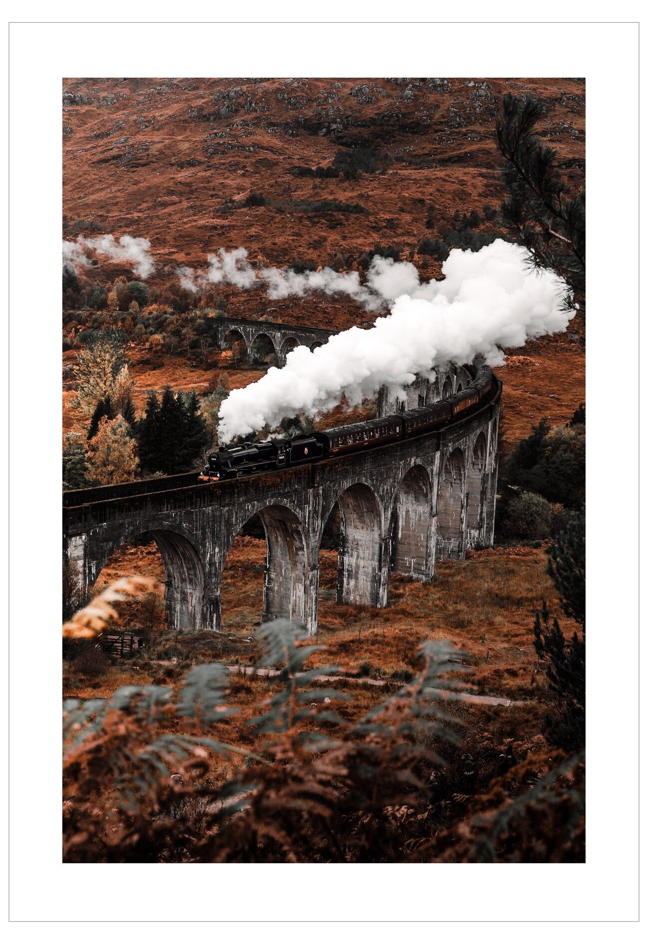 Steam train on a viaduct with steam billowing into the air, set against a scenic landscape.