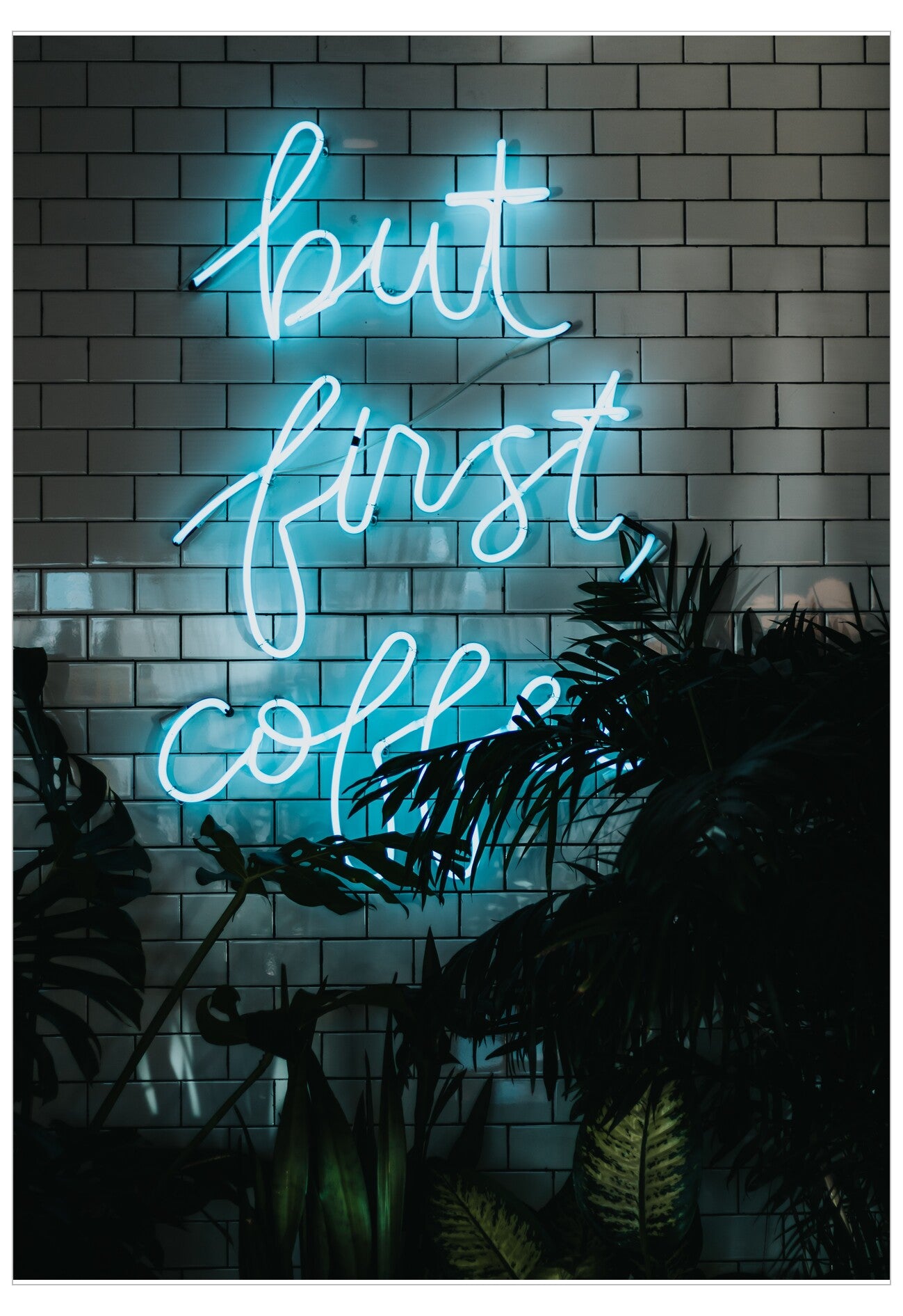 Neon sign with 'but first, coffee' text on a brick wall with plants.