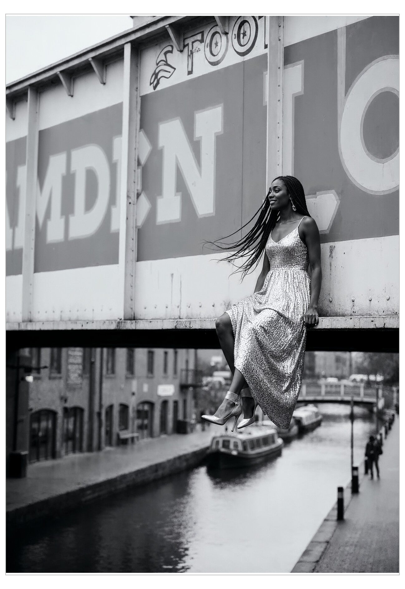 Woman in a patterned dress sitting on a bridge over a canal with 'Camden' signs in the background.