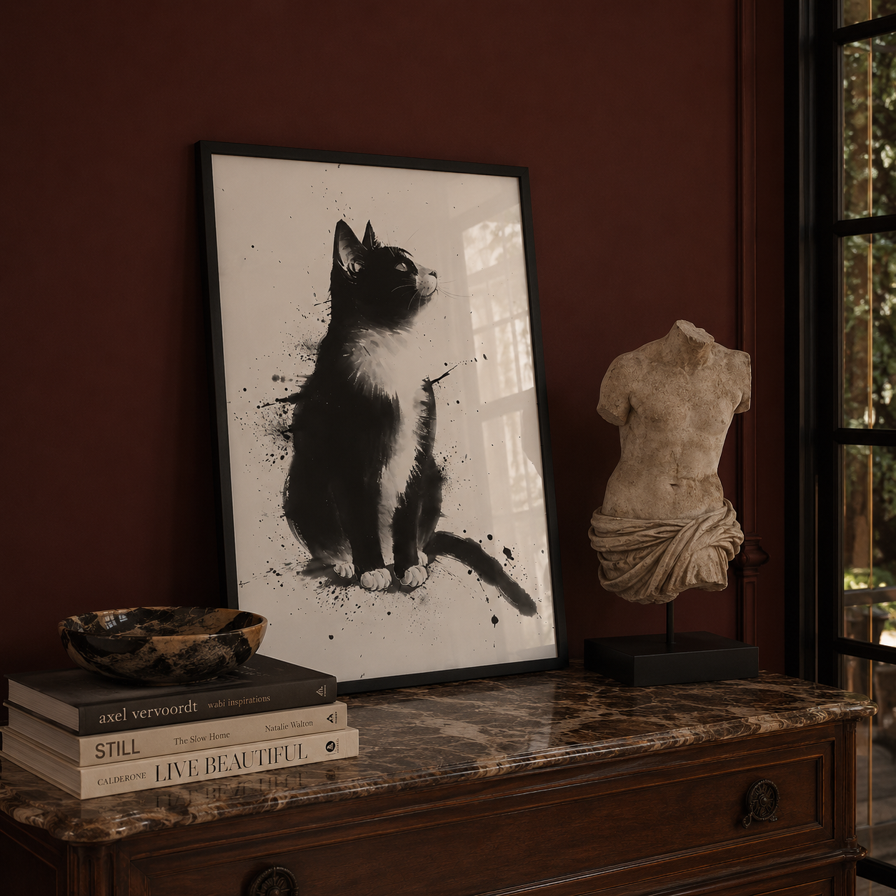 Framed artwork of a cat on a marble surface with books and a statue.
