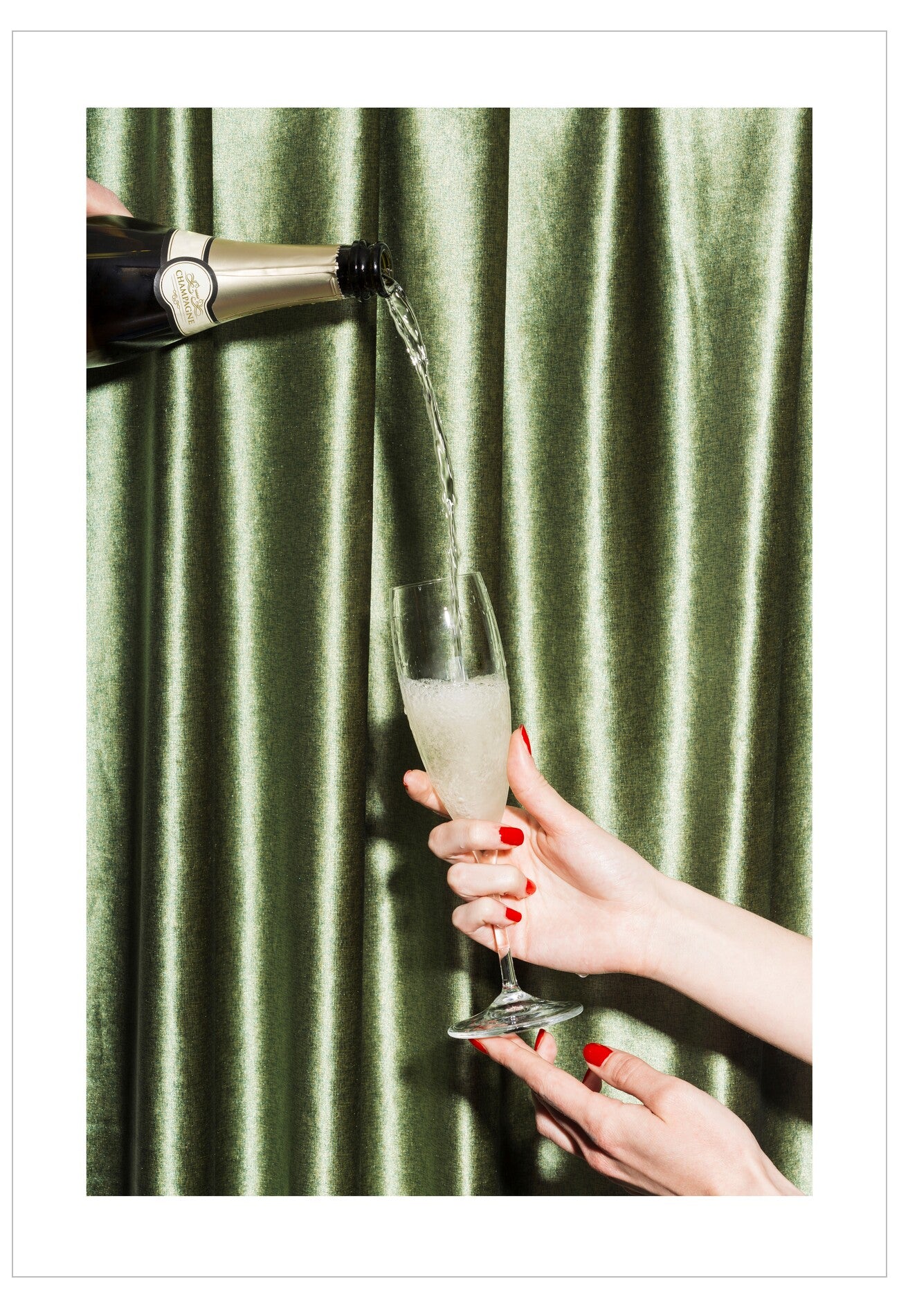 Champagne being poured into a glass held by a hand against a green curtain background