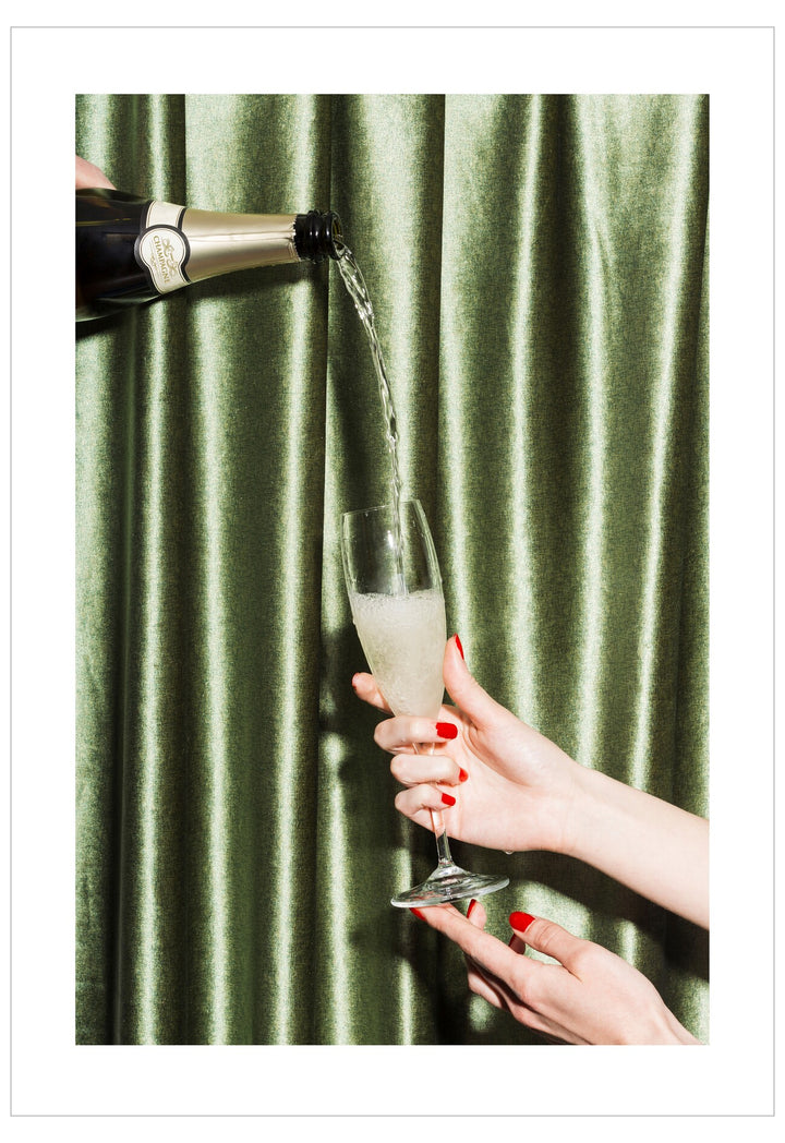 Champagne being poured into a glass held by a hand against a green curtain background
