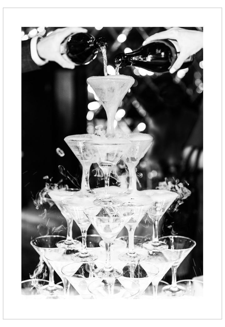 Champagne being poured into a pyramid of martini glasses with a blurred festive background.