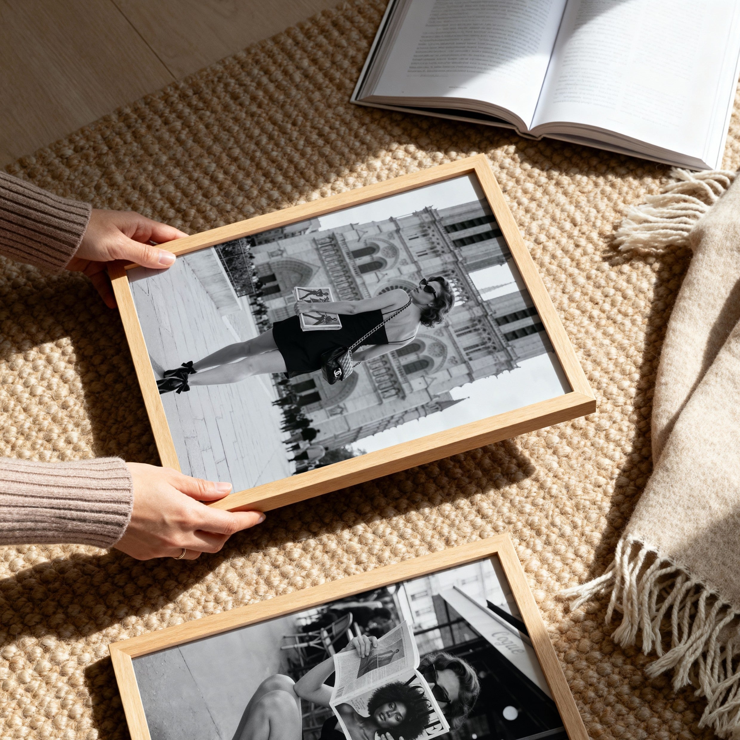 Person holding a framed black and white photo on a textured surface with another frame and book nearby.