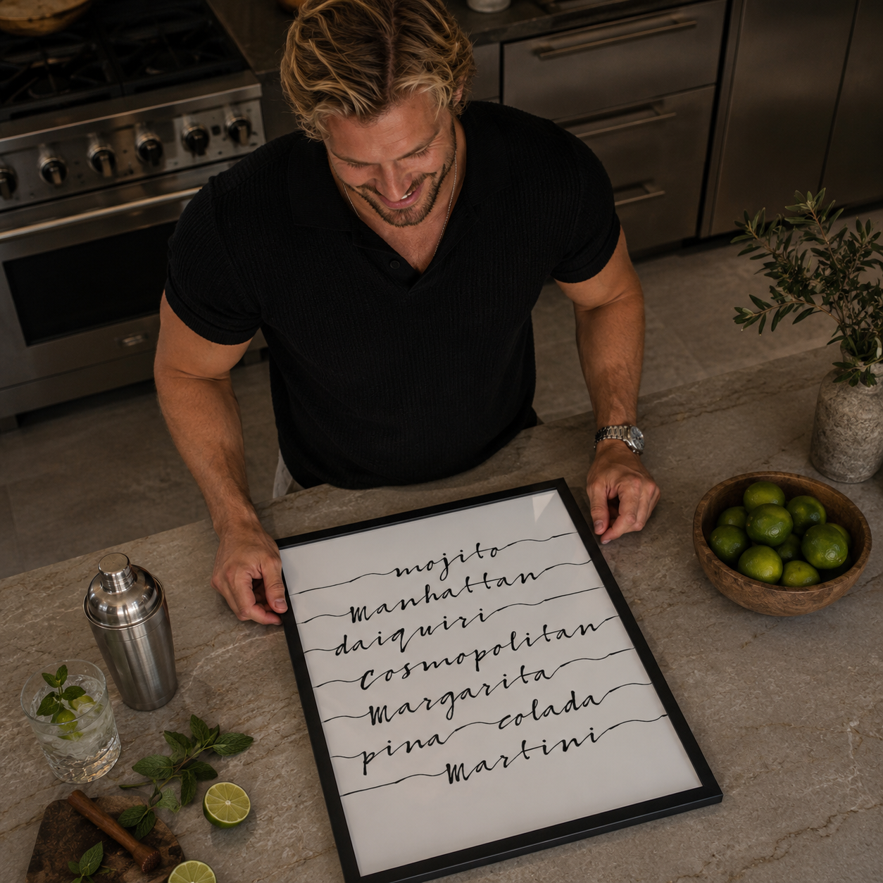 Man in a kitchen holding a framed list of cocktail names with limes and a cocktail shaker on the counter.