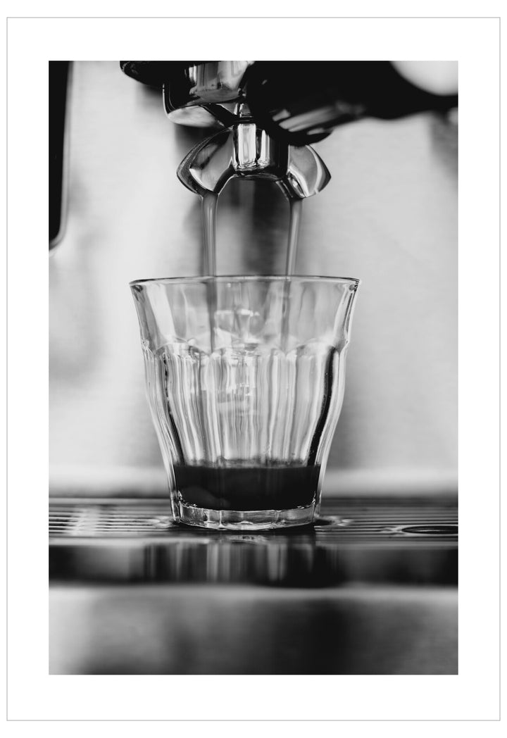 Black and white photo of an espresso being poured into a glass.
