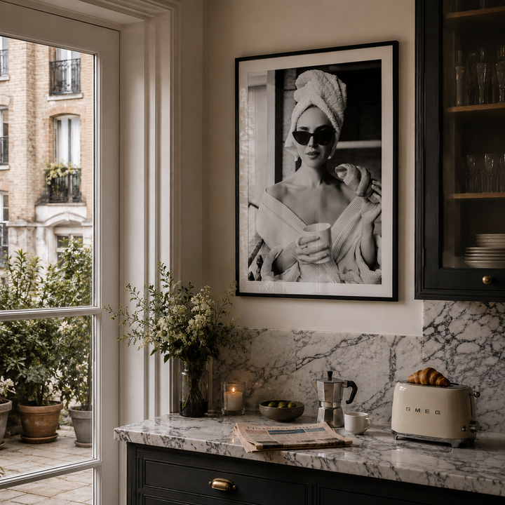 Kitchen interior with a framed black and white portrait on the wall, marble countertop, and window view.
