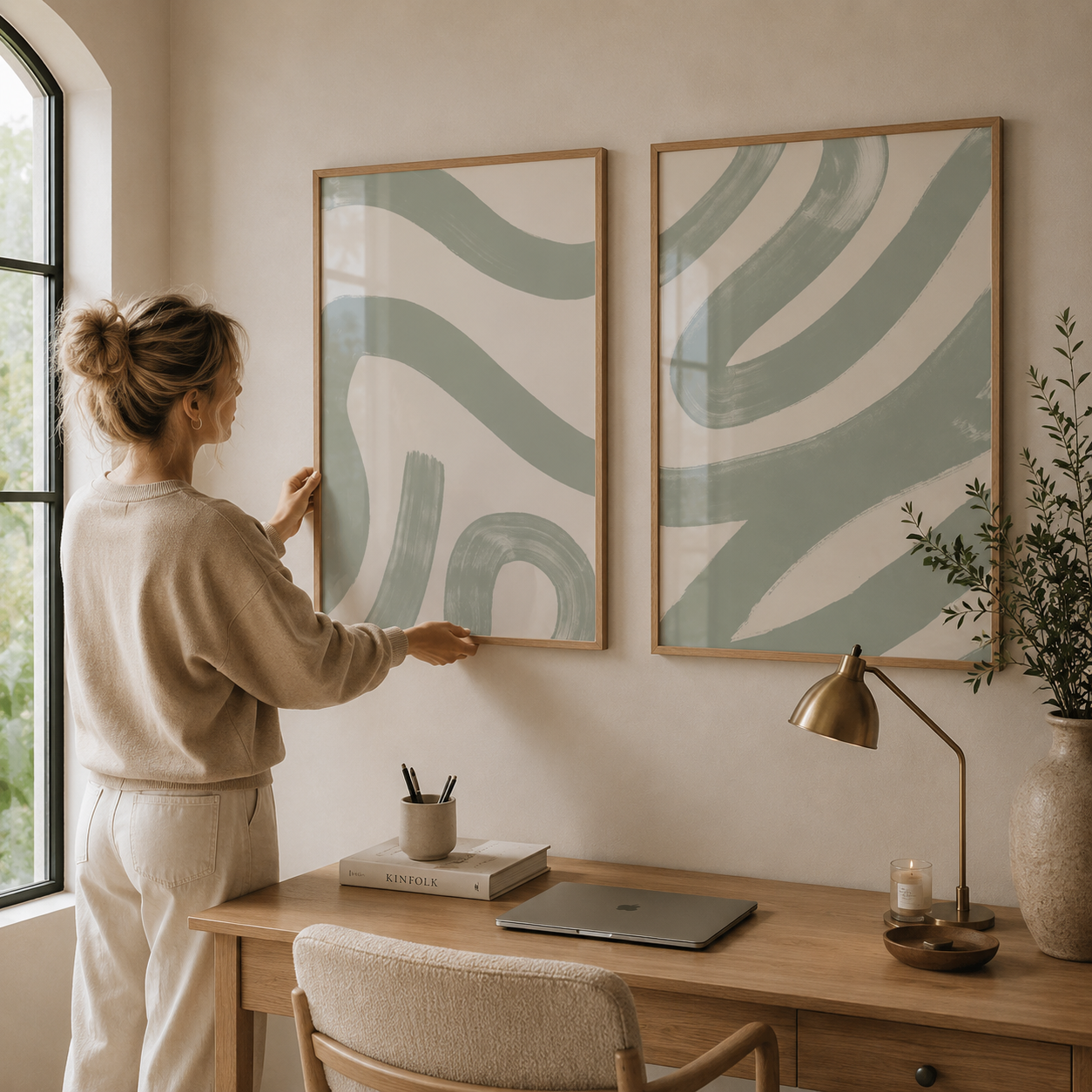 Woman hanging green abstract art on a wall in a home office setting