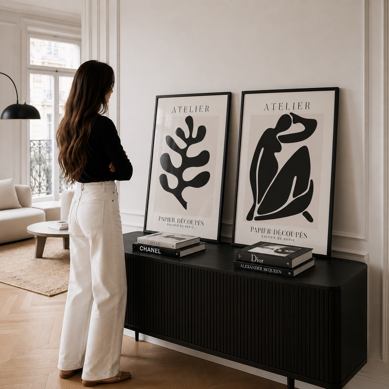 Woman standing in a modern living room with black and white framed art on a console table.