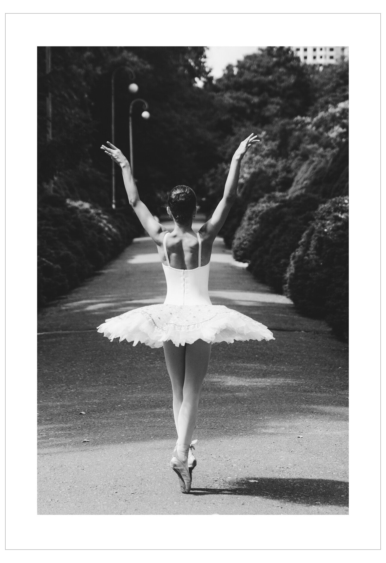 Ballerina in a white tutu standing on one leg with arms outstretched in a park setting.