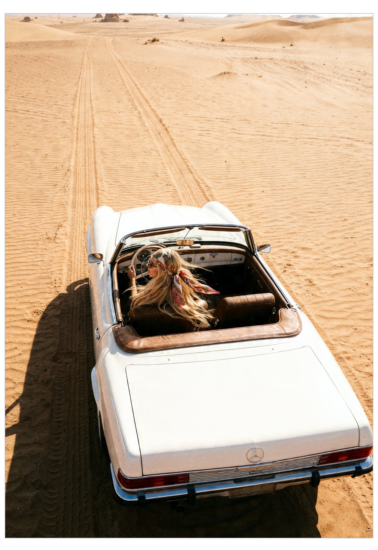 White convertible car in a desert setting with a person sitting inside.