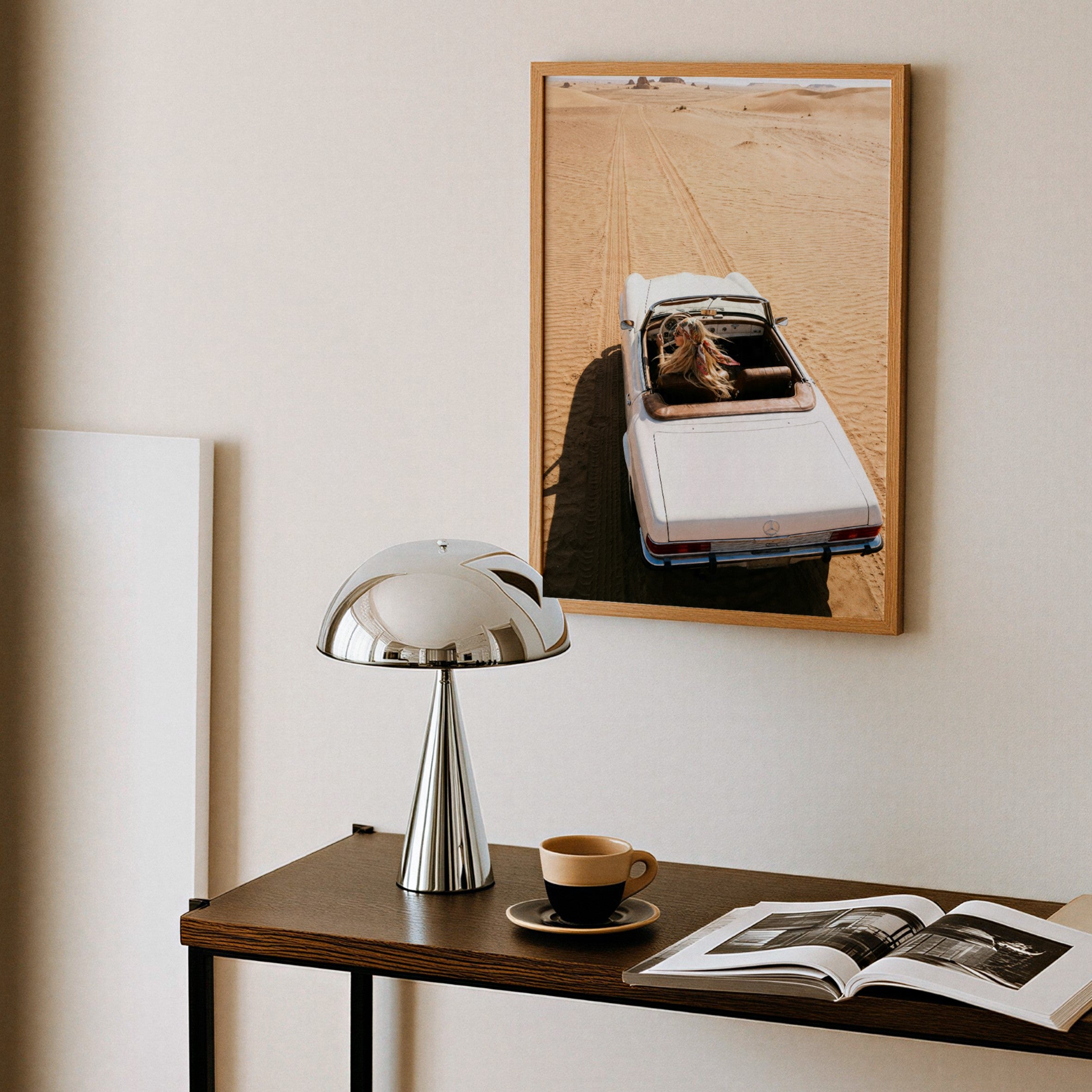 Table with lamp, coffee cup, and open book, wall art of a car on a road.