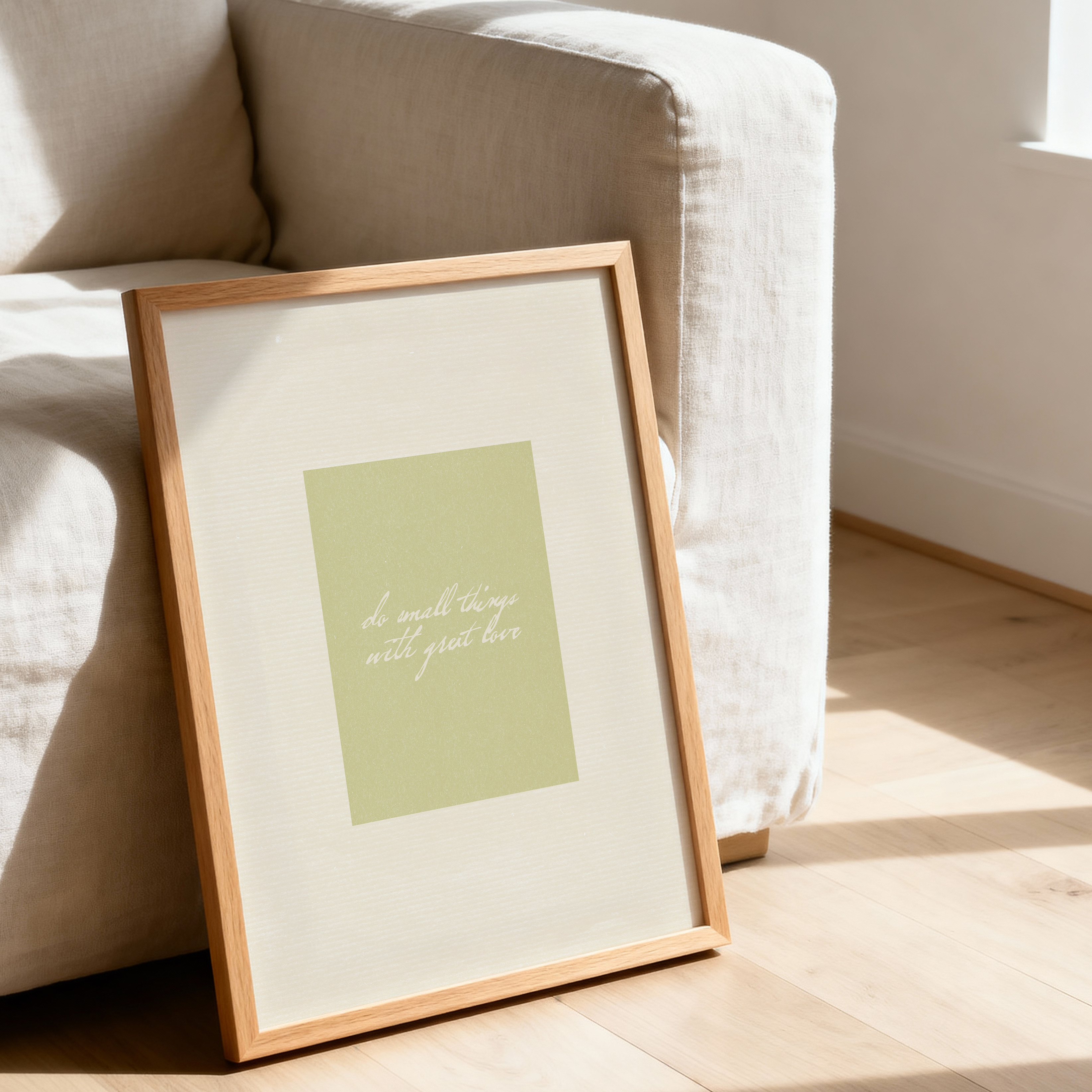 Framed neutral artwork on a wooden floor with a beige sofa in the background