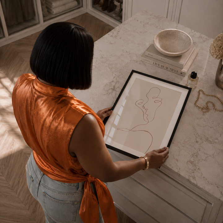 Person in an orange top holding a framed artwork on a marble surface.