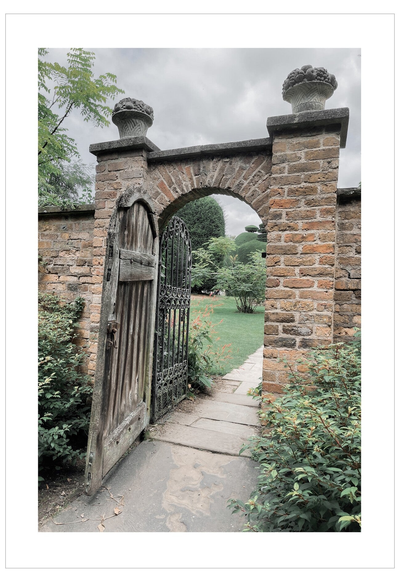 Worn wooden gate in a stone archway with overgrown grass and plants.