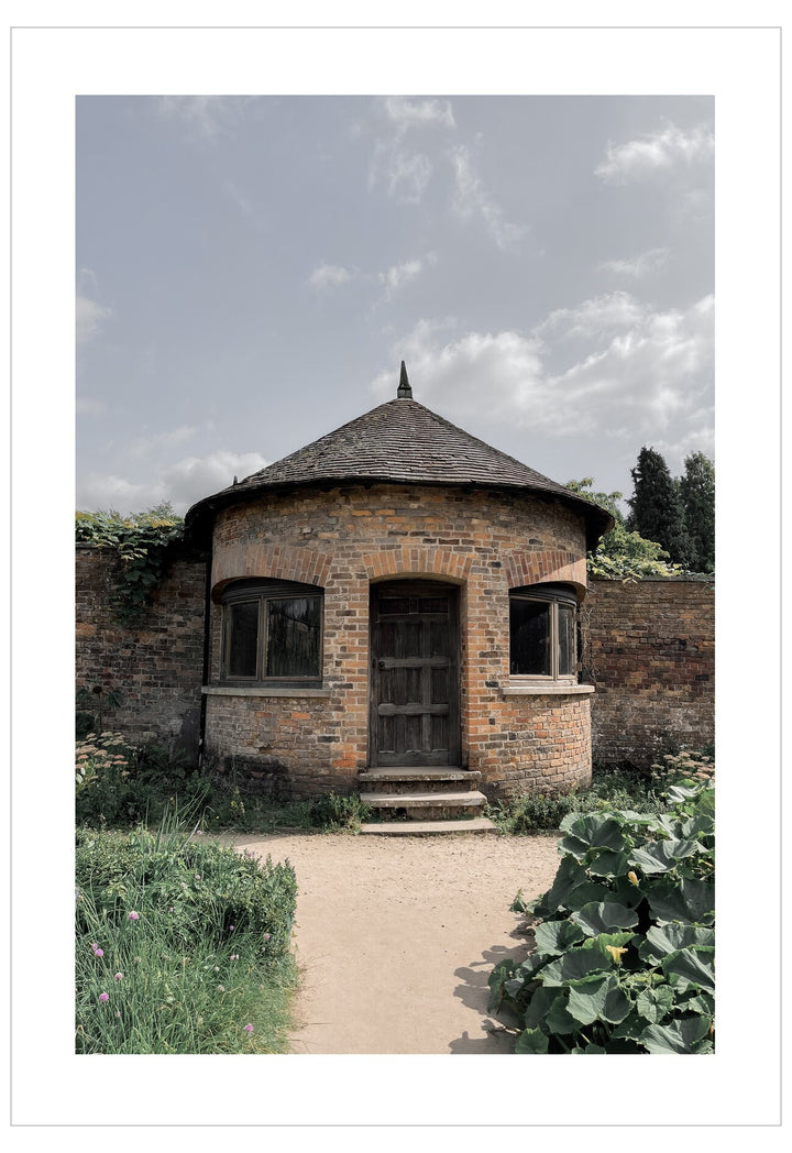 Round brick building with a thatched roof in a garden setting