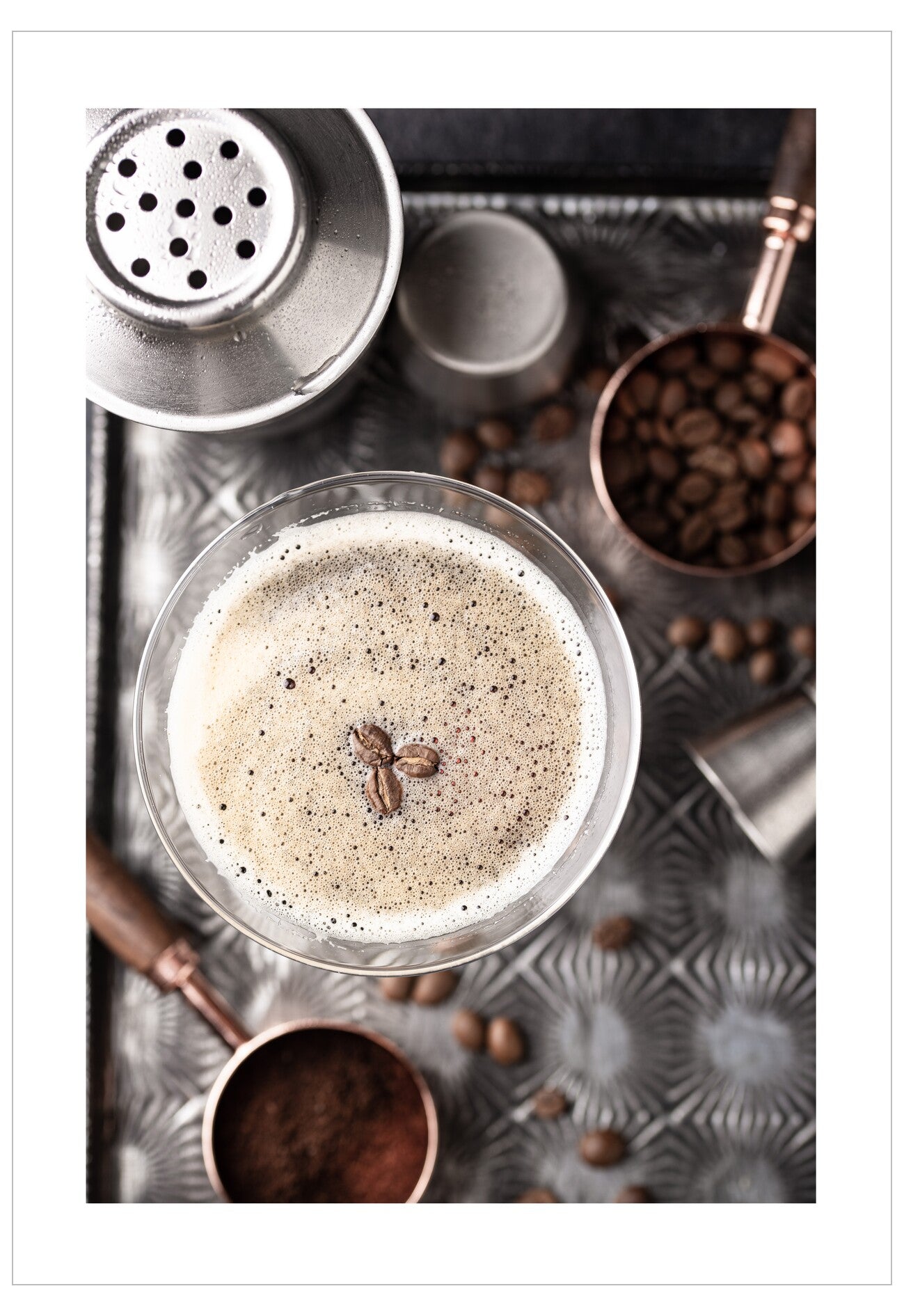 Glass of coffee cocktail with coffee beans on a textured metal tray