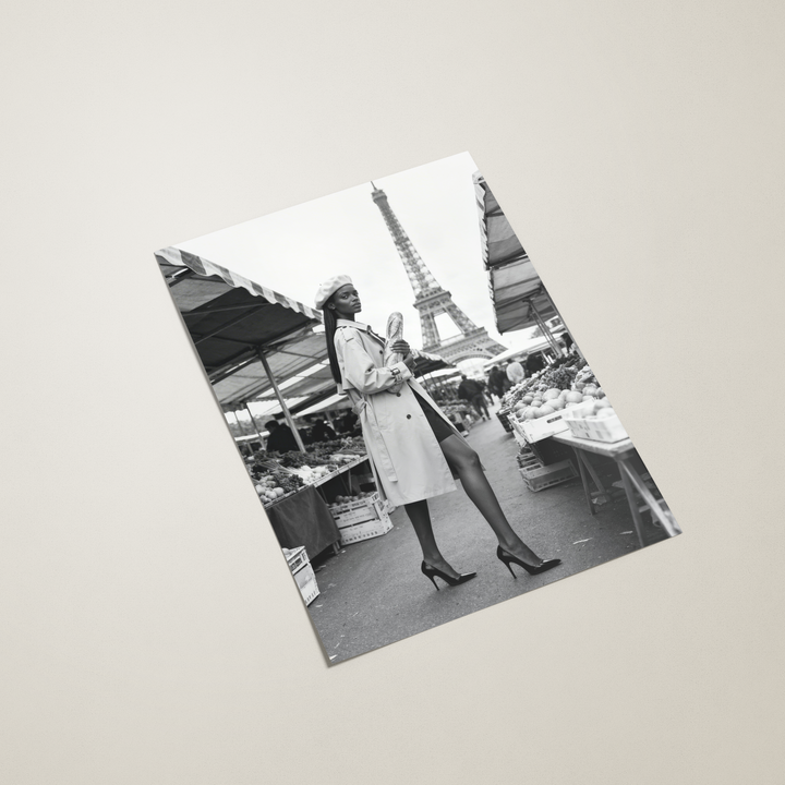 Black and white photo of a woman in a coat with the Eiffel Tower in the background on a light gray surface.