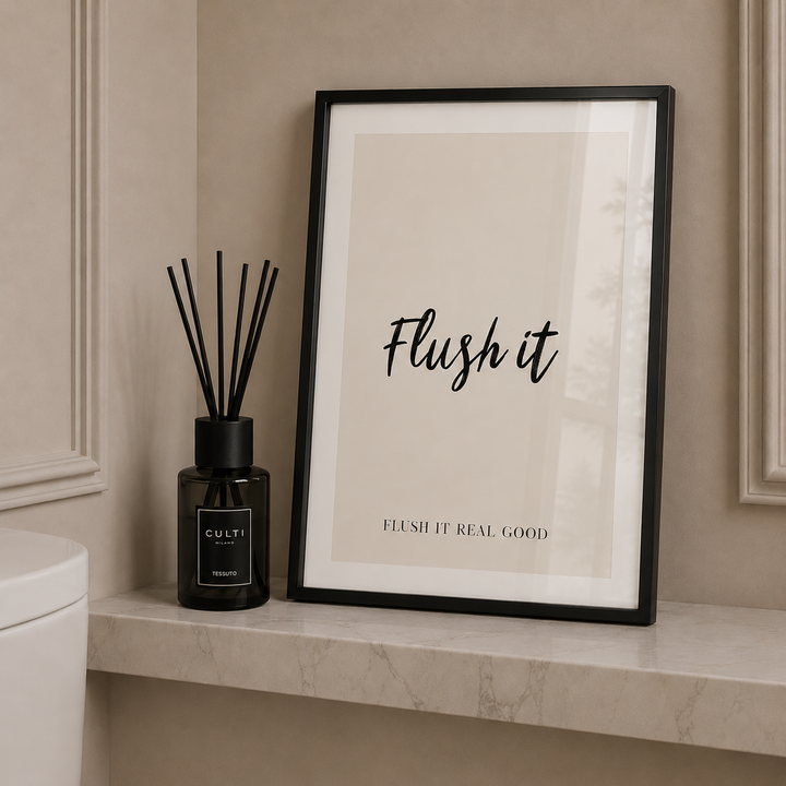 Framed print with 'Flush it' text on a bathroom shelf next to a diffuser.