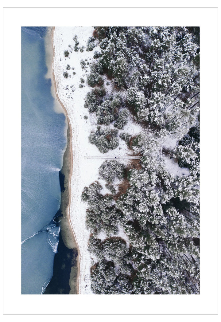 Aerial view of a snowy landscape with trees and a body of water.