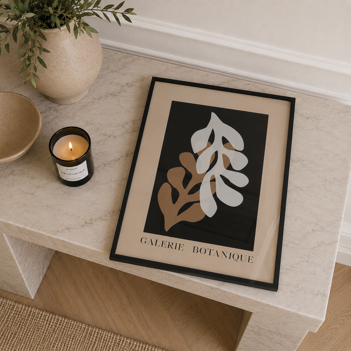 Framed artwork with leaf design on a table next to a candle and plant