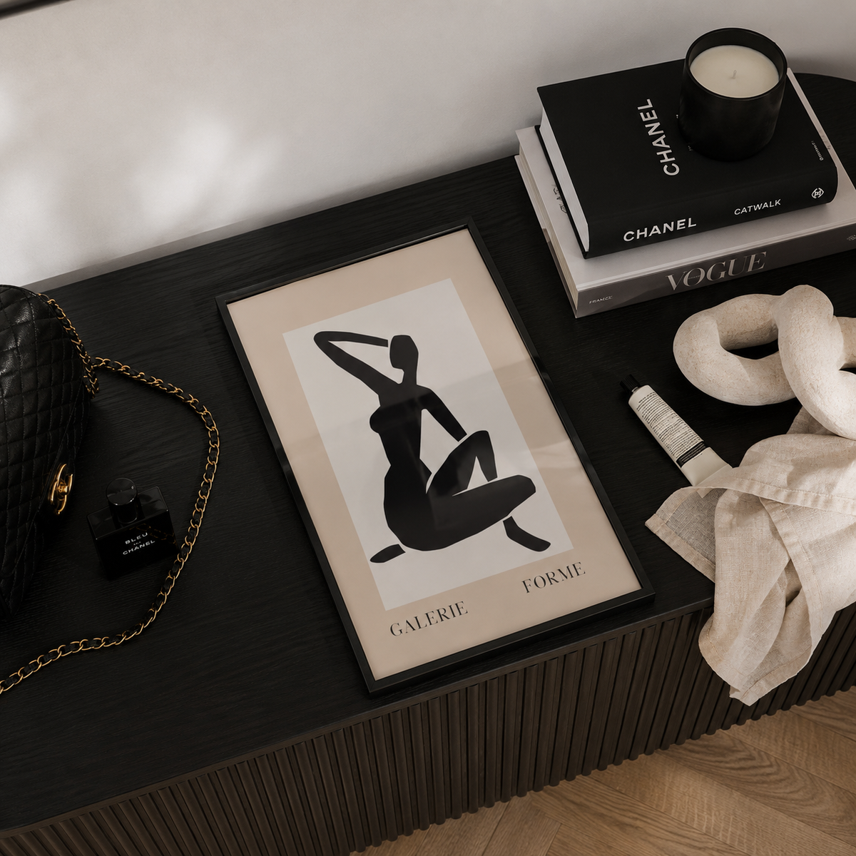 Framed art print on a dark wooden surface with a Chanel book and candle.