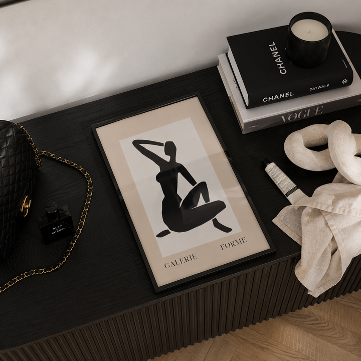 Framed art print on a dark wooden surface with a Chanel book and candle.