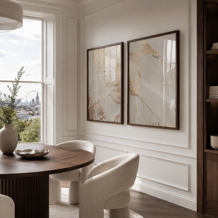 Modern dining room with a round wooden table and white chairs, featuring two framed artworks on the wall.