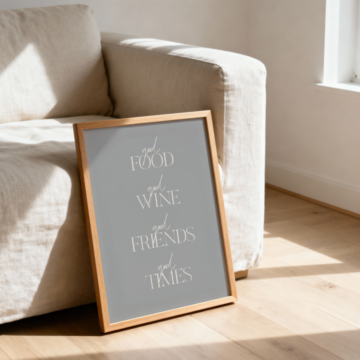 Framed poster with 'Good Food Good Wine Good Friends Good Times' text on a wooden floor next to a beige armchair.