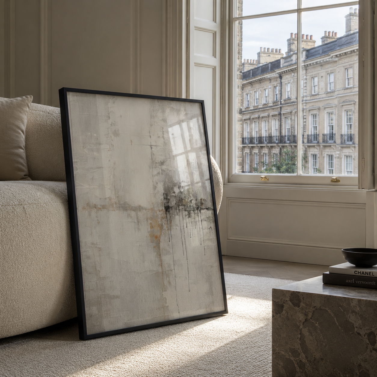 Framed abstract art leaning against a wall in a living room with a window view.