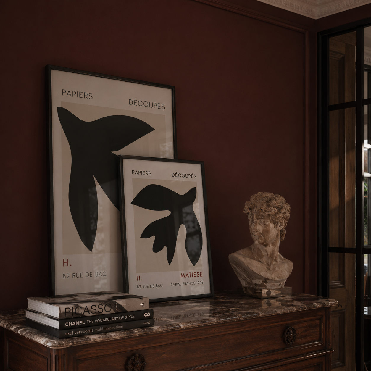 Framed artworks and a bust on a marble surface with a dark wall background