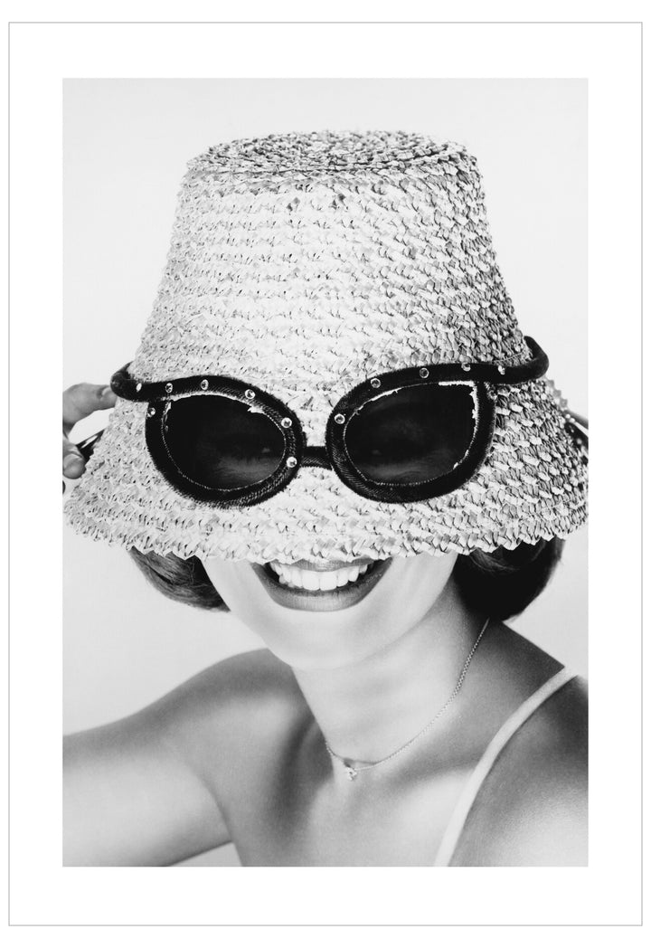 Black and white photo of a person wearing a decorative hat with sunglasses on top